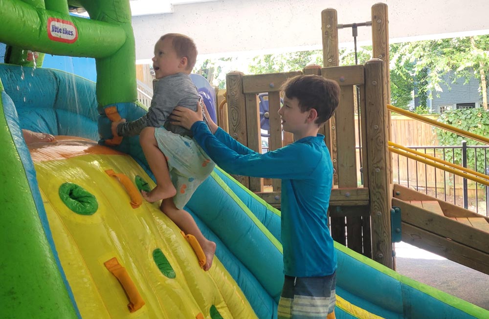 Boy helping young baby up a bouncy wall