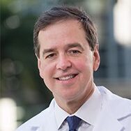 Dr. John Niparko in a white lab coat with a tie