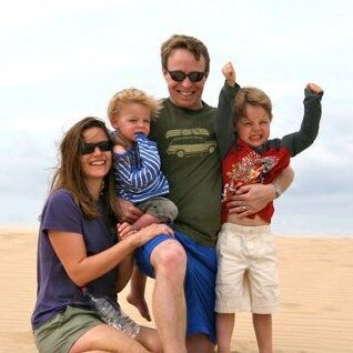 A man and woman with sunglasses on the beach with their two young children